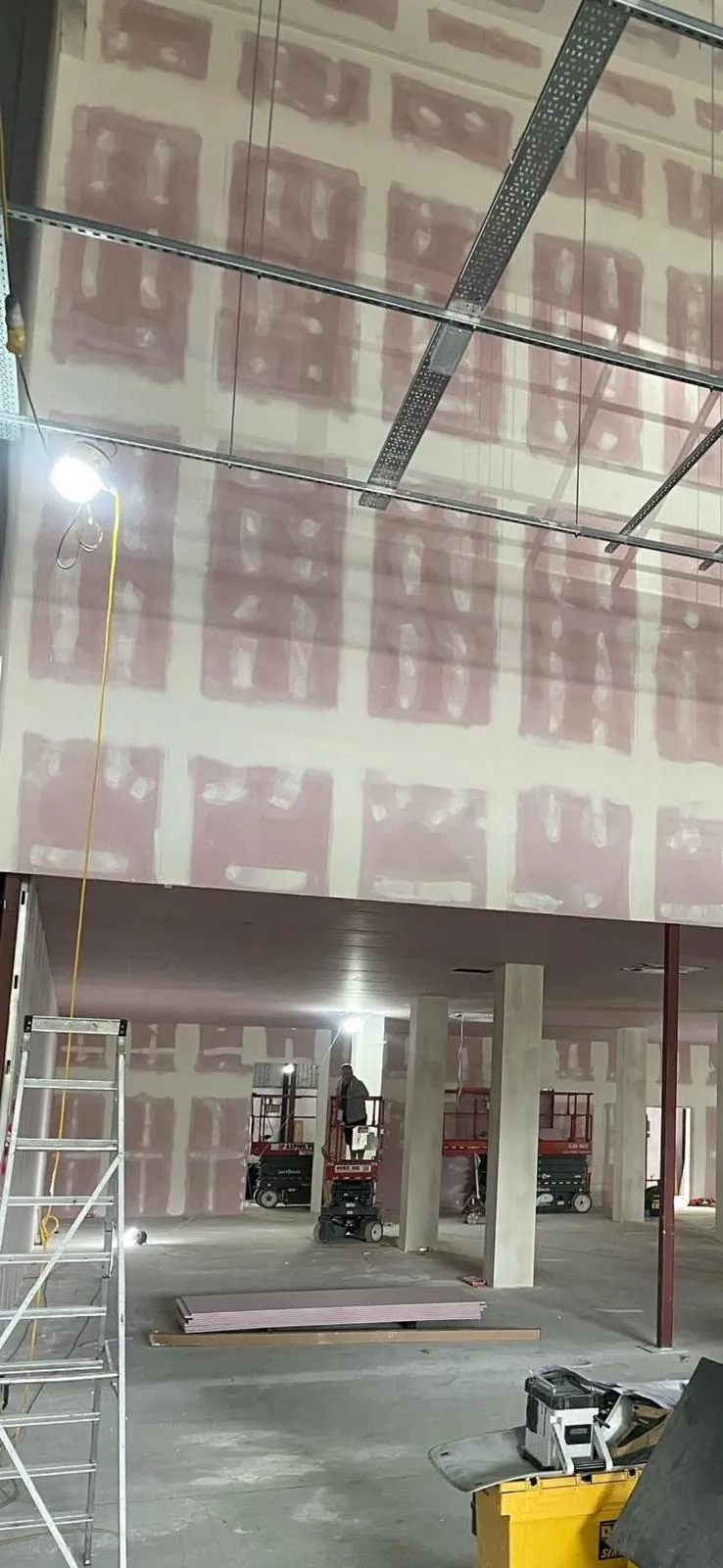 Double height taped and jointed plasterboard wall above a mezzanine with scissor lifts below