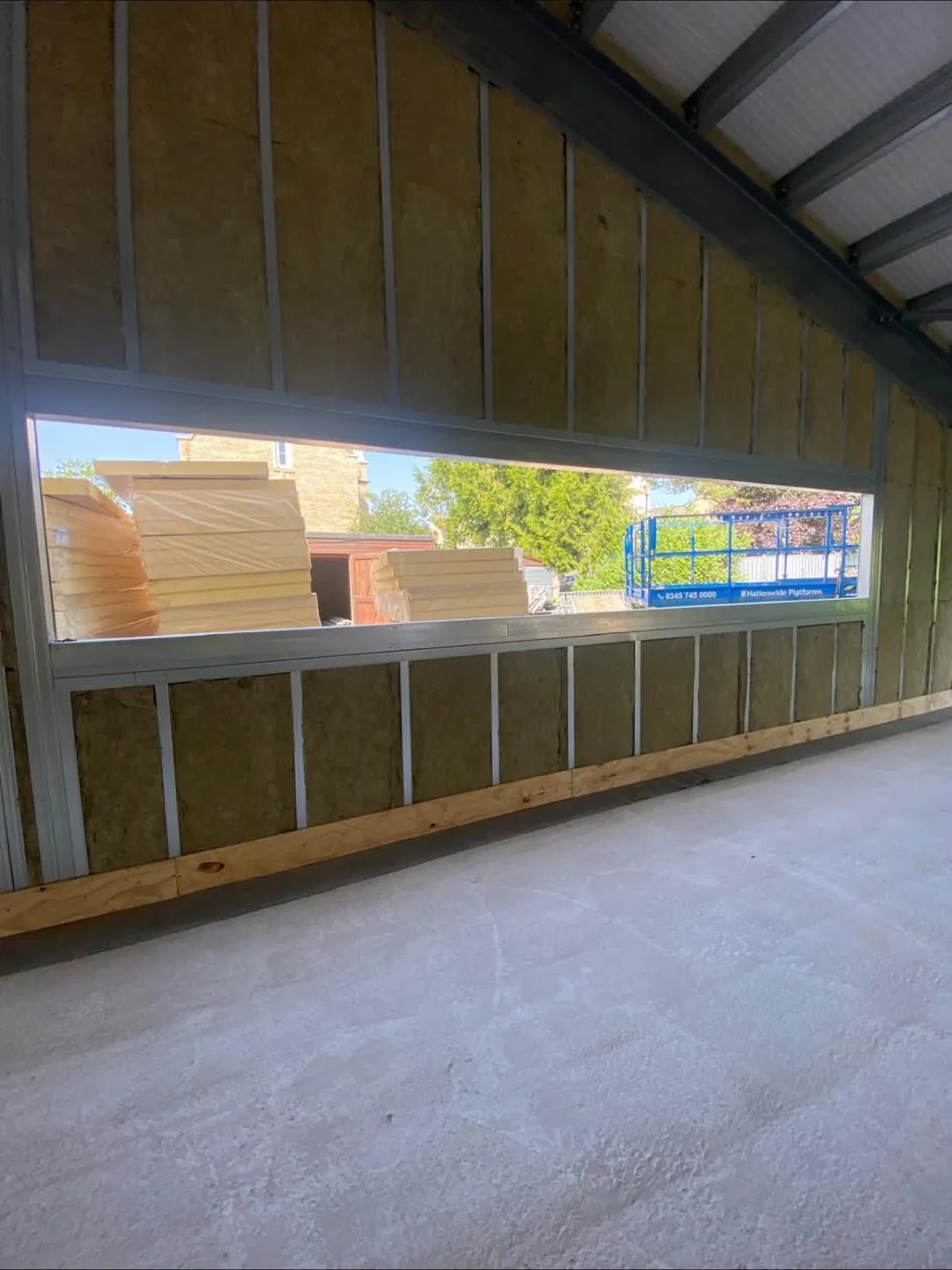 Metal stud wall with mineral wool insulation fitted between studs around a long ribbon window